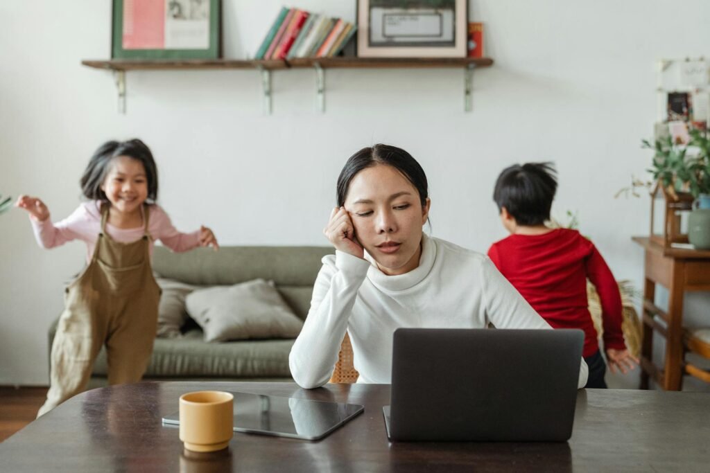 Woman looking exhausted while trying to work with kids playing around